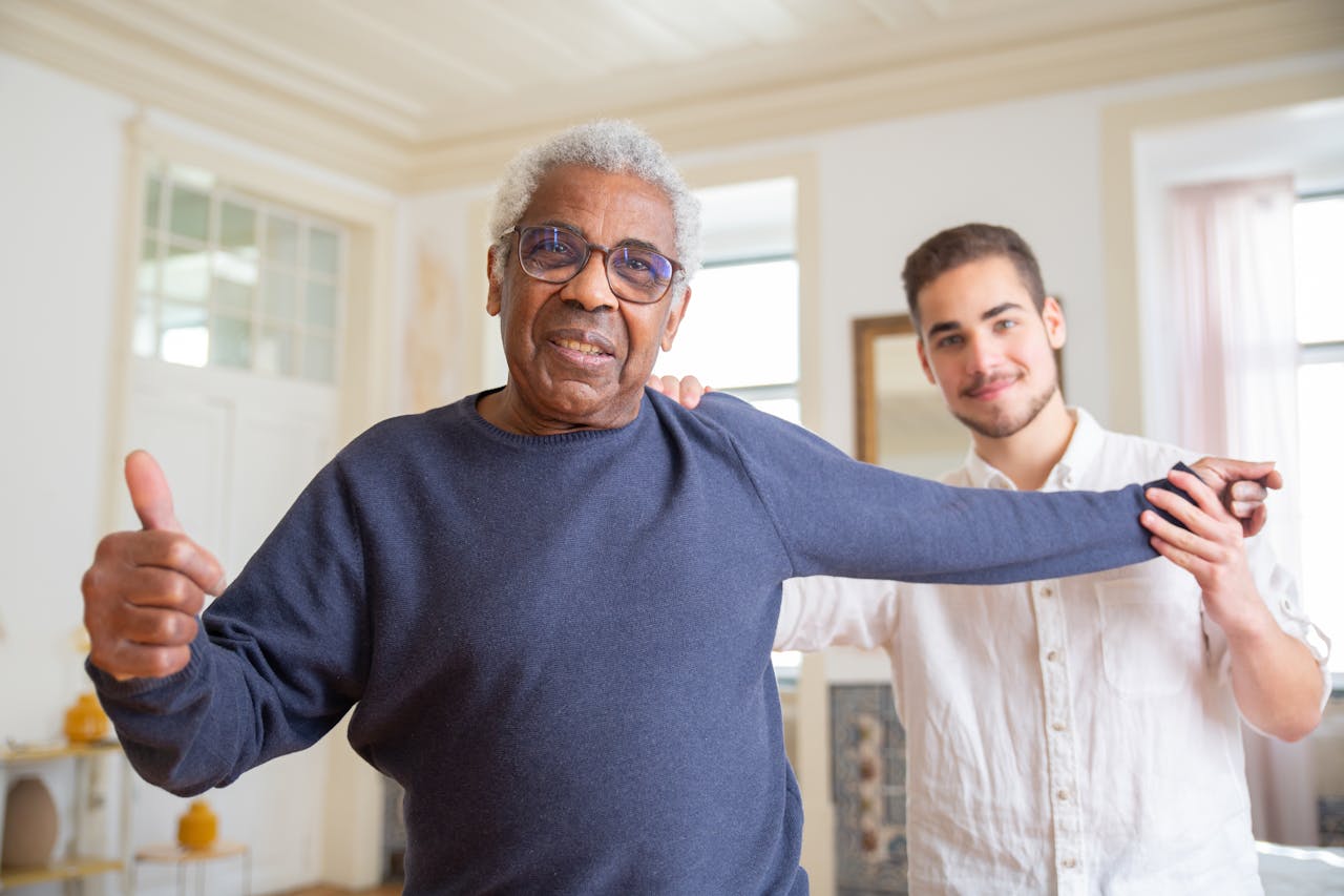 Elderly man smiling with caregiver in a supportive home environment, promoting health and happiness.
